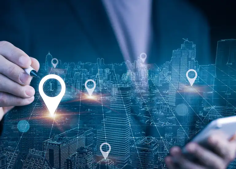 Businessperson using stylus and smartphone with digital city map and location markers.