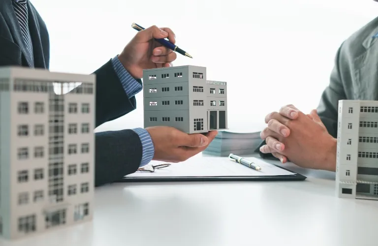 Two professionals in suits discussing a gray building model over a white desk with documents.