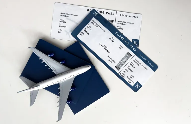 Two boarding passes, a dark blue passport, and a small airplane model on a white surface.