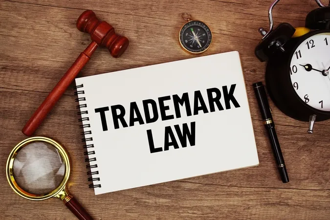 Spiral notebook with "TRADEMARK LAW" text, wooden gavel, magnifying glass, compass, black pen, and alarm clock on wooden surface.
