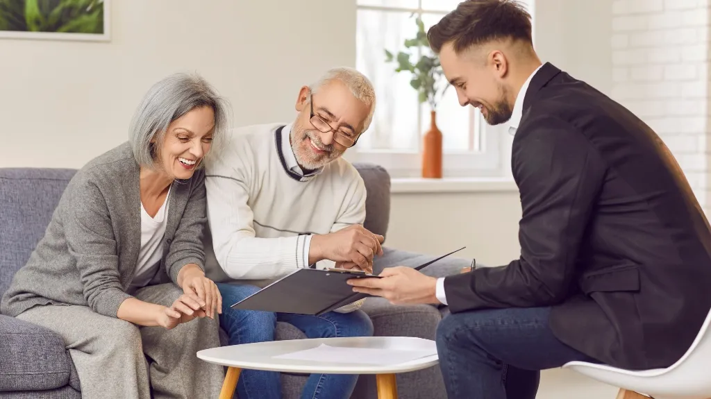 Three adults, an older couple and a young man, reviewing documents in a bright living room.