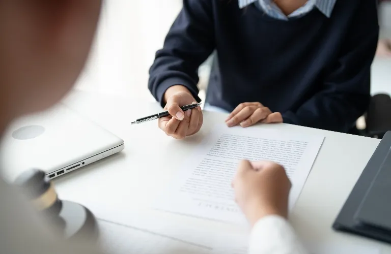 Two individuals in a professional setting reviewing a document at a white desk.